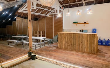Rustic outdoor bar and seating area with bamboo accents, picnic tables, and warm pendant lighting.