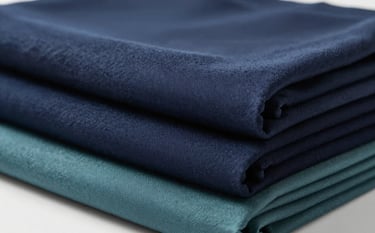 Premium textile fabrics neatly stacked, showcasing sophisticated textures and patterns. Professional studio lighting, establishing a refined professional image. Incorporates navy #283645 and teal #5B7B7C tones.