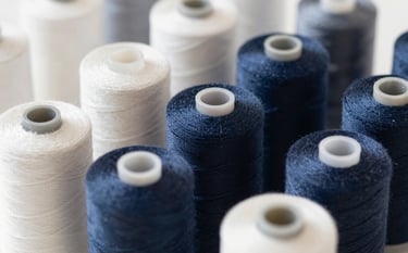 High-quality sewing thread spools arranged perfectly. Trustworthy and modern aesthetic. Soft lighting, sophisticated look. Colors include off-white #F7F7F2 and navy #283645.