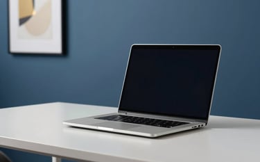 A minimalist tech-focused shot of a sleek silver laptop on a clean white desk. In the background, a steel blue wall is decorated with a framed abstract print in soft gold. The atmosphere is quiet, secure, and modern.