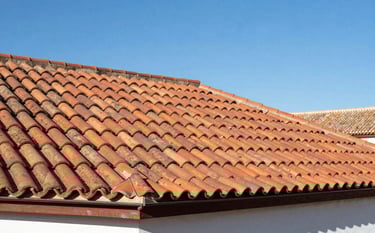 Photography of a completed residential roof restoration featuring traditional terracotta tiles against a bright blue sky. The scene is set in a Southern European Spanish town. The roof looks sturdy, clean, and perfectly finished, showcasing unwavering reliability.