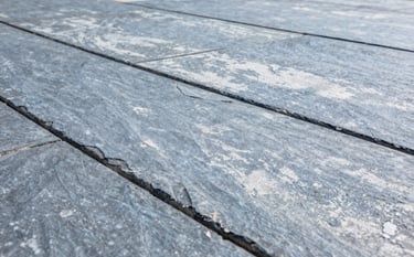 A close-up photograph of a precision-stamped concrete patio with a slate texture. The concrete has a clean, Steel Blue Grey and Soft Cloud White finish. The composition is sharp, showing the intricate grout lines and texture under bright, natural daylight, reflecting robust reliability.