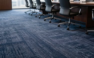 Close-up of premium office moquette being installed in a luxury corporate boardroom in Riyadh. The carpet has a sophisticated texture with deep blue-grey tones matching #1C2833. Natural light hits the floor, emphasizing the high-quality fibers and professional finish.