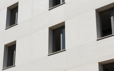 A close-up photograph of a clean, modern building facade in Southern Europe being renovated with white high-density EPS insulation panels. Professional construction site, bright daylight, showcasing a sophisticated and efficient installation process with a focus on precision and responsibility.