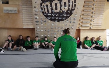 a man in a green jacket sitting in a front of a climbing wall