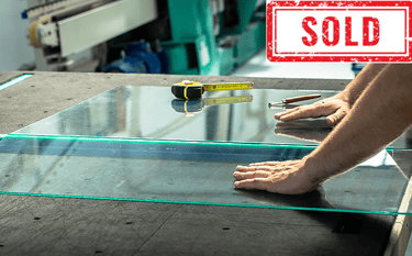 Worker measuring and handling glass sheet on a table, labeled "SOLD".