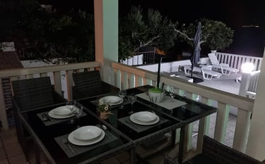 The photograph shows the apartment balcony with a dining set at night.