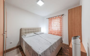 The photo shows a bedroom with a double bed, wardrobes, a chest of drawers and a floor fan.