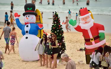 a group of people standing around a christmas tree at the beach in Australia, Christmas celebration
