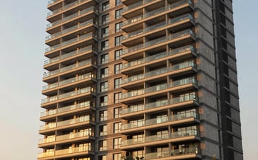 A high-end residential high-rise apartment complex in Gurgaon during golden hour. The architecture is modern with sleek glass balconies. The lighting is warm and sophisticated, using golden tan tones from the palette. South Asian / Indian setting.