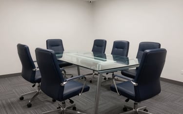 Photography of a modern boardroom in Lahore with clean lines and ergonomic dark navy blue chairs around a glass table. The atmosphere is professional and quiet, with a palette of slate grey and soft off-white.