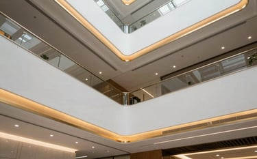 Architectural shot of a modern multi-level white false ceiling in a professional South Asian office lobby. Subtle recessed lighting and gold-painted cove accents create a sophisticated, luxury atmosphere. Sharp geometric lines and professional minimalist styling.