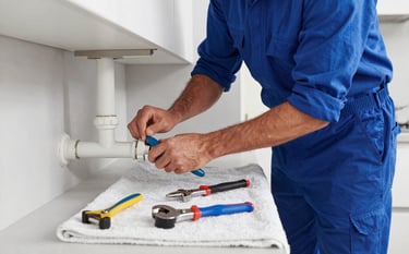 A professional plumber in a modern Northern European / German / Hamburg kitchen, wearing a Deep Ocean Blue uniform, fixing a pipe leak. Modern tools are laid out neatly on a Mist White towel. Bright, clean lighting, high-end photography.