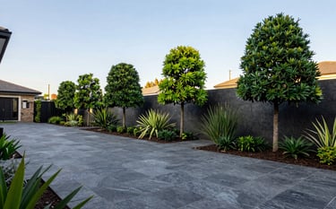 Professional landscaping and maintenance in a Southern African residential garden. Wide shot showing neat paving stones and perfectly trimmed trees. The aesthetic is sharp and clean, featuring dark charcoal grey stone textures and vibrant greenery under a clear sky.