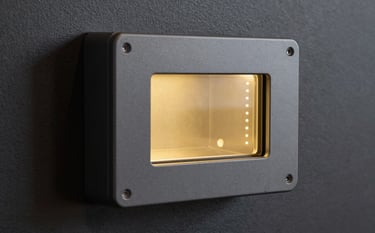 Close-up of a premium biometric security terminal with a sleek slate grey finish, featuring an antique gold glowing scanning surface, mounted on a deep charcoal textured wall.