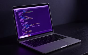 A high-end professional laptop on a dark desk in a dimly lit room, with lines of code displayed on the screen glowing in electric purple and deep purple. Soft cinematic lighting with deep navy shadows.