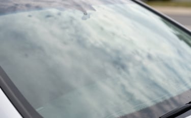 A detailed close-up of a flawless, newly repaired windshield reflecting a bright North American sky and soft off-white clouds. The image emphasizes clarity, safety, and perfection. The composition is clean and minimalist, showing the high-quality finish of the glass.