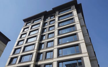 A low-angle exterior shot of a stunningly modern, high-end residential building in North American / US. The facade features charcoal grey accents and off-white stone under a clear steel blue sky.
