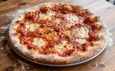 A close-up, high-angle photograph of an artisanal pizza on a rustic wooden table in a North American restaurant. Soft natural light highlights the texture of the flour and the deep ripe crimson of the tomato sauce. The composition is clean and minimalist, reminiscent of Scandinavian design.