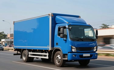 A sleek, modern delivery truck painted in corporate ocean blue driving along a clean, sunlit road in a West African / Ghanaian city. The composition is dynamic, showing movement and reliability. The sky is a clear soft sky blue.