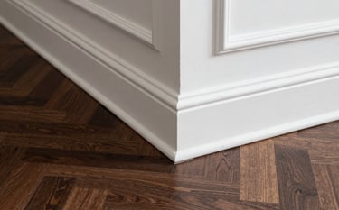 A detailed architectural photograph of high-end white crown molding meeting a dark walnut herringbone patterned floor. The shot showcases exquisite trim work and sophisticated design in a luxury North American residence.