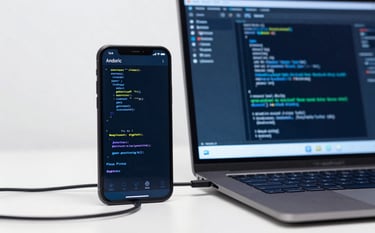 A close-up photograph of an Android development environment in a bright North American studio. An Android device is connected to a laptop showing lines of code. The workspace is clean, featuring Alice blue and deep blue tones, signifying technical prowess.