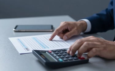A close-up of a professional's hands reviewing tax documents and a financial calculator on a sleek surface. The environment is minimalist and efficient. Deep blues of #1C2B3C and highlights of #F5F8FA create a mood of accuracy and serious financial compliance.