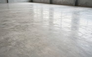 A wide, low-angle shot of a newly finished, polished industrial concrete floor inside a large warehouse in Brazil. The floor reflects soft off-white light, showcasing a professional, high-durability finish. The atmosphere is clean and industrial.