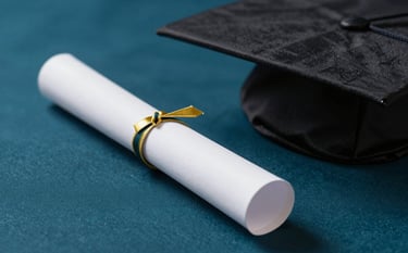 A close-up, high-prestige photograph of a graduation scroll and a mortarboard resting on a dark teal textile surface (#0A2B2E). The lighting is soft and focused, evoking a sense of achievement and reputable academic tradition. Small accents of gold #B48C5B are visible in the scroll's ribbon.