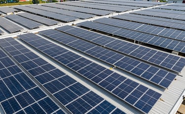 Large-scale industrial factory roof in a Thai industrial estate covered in a vast array of high-quality solar panels. Cinematic wide-angle photography showing the scale of the clean energy project under a bright sun.