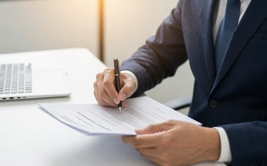 A close-up of a professional East Asian / Chinese legal expert’s hands reviewing formal Australian migration documents. The setting is bright and authoritative, featuring warm golden lighting and minimalist office decor that projects trust.