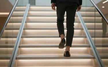 Close up of a luxury glass and steel staircase where the bottom two steps are lighting up sequentially as a foot approaches. Modern, high-tech, and safe aesthetic. Clean composition featuring #B28D69 highlights.