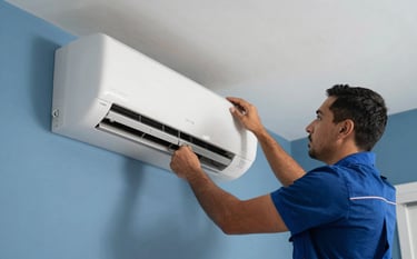 A technician in a Latin American / Spanish residential setting installing a white modern air conditioning unit on a wall. The technician is focused and professional. The lighting is crisp, highlighting the clean medium blue and sky blue tones of the room and tools.