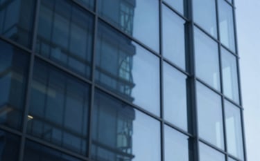 Abstract and sophisticated composition of blue architectural glass reflecting light. The image represents stability, structure, and professional transparency. Shades of #0A1C29 and #2E5C6E dominate the reflection, creating a trustworthy brand visual.