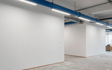 Interior shot of a modern office space undergoing renovation. High-quality finishing on white walls, visible steel blue conduits, and clean, bright interior lighting. The shot emphasizes precision and minimalist design in interior finishing.