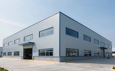 Wide-angle shot of a large-scale commercial warehouse construction. The building features light blue-grey cladding and modern industrial design. The lighting is bright and natural, highlighting the sophisticated and clean aesthetic of AE construction's industrial projects.