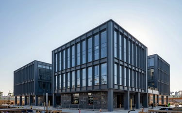 Architectural photography of a modern administrative building under construction. The structure shows clean lines with steel blue and dark slate grey beams against a bright, clear sky. The environment is orderly and professional, reflecting a minimalist and reliable construction site.