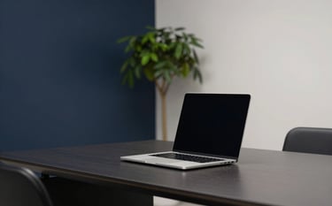 A high-end, minimalist office workspace with a sleek laptop open on a desk. The lighting is soft and professional, with deep navy and soft off-white tones in the room decor. A small forest green plant sits in the background, out of focus.