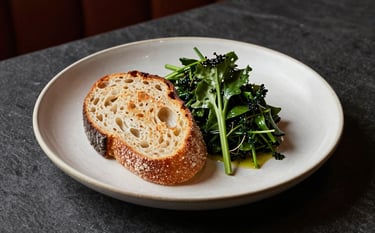 High-end photography of a beautifully plated rustic dish in a North American / US Scandinavian-style restaurant. Warm lighting highlights textures of fresh bread and greens. Crisp Parchment ceramic plate on a Dark Slate table.