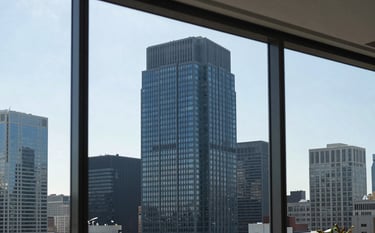 A modern US skyscraper skyline visible through a clean, sophisticated office window. The indoor setting features architectural details in dark blue and grey-blue, suggesting an authoritative and established corporate firm.