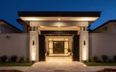 Sleek architectural photography of a contemporary South American luxury residence at dusk. Discreet security sensors and a high-end gated entrance are visible under warm exterior lighting. The atmosphere is one of profound safety and tranquility, with the deep night sky in navy and slate blue shades.