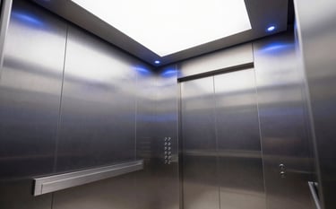 Interior of a modern, sleek elevator cabin with silver brushed metal panels and soft blue LED accent lighting. Clean lines and professional architectural photography style in a South American corporate building.