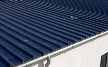 Modern French architecture showing a perfectly maintained roof with dark blue tiles and clean silver gutters. The composition is sharp and high-contrast, conveying modern efficiency and durability.