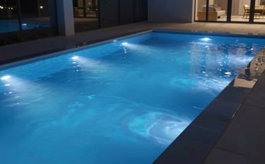 An innovative pool at night, illuminated by vibrant blue LED underwater lights. The water is crystalline, and the surrounding deck is sleek and modern, reflecting the professional mood and #0D1B2A palette.