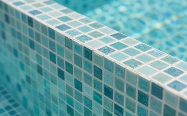 Close-up of premium turquoise mosaic tiles being meticulously installed in a modern swimming pool. The lighting is crisp, highlighting the clean lines and sophisticated craftsmanship, incorporating brand tones of #415A77 and #E0E1DD.