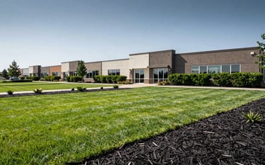 A wide-angle landscape photograph of a pristine commercial property in the US with vibrant green lawns, freshly installed dark mulch in flower beds, and perfectly trimmed hedges. Professional and trustworthy aesthetic.