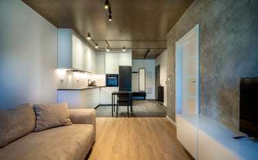 Nowoczesny salon z aneksem kuchennym, jasne meble, betonowy sufit i ściana TV.