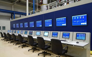 A high-tech industrial control room in a modern power plant with glowing blue screens and indicators. The atmosphere is professional and innovative, reflecting leadership in electrical engineering. Professional lighting in a Spanish / Global setting, dominated by dark blue and off-white tones.
