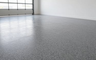 A professional wide-angle shot of a clean modern garage with a high-gloss flake epoxy floor. The floor features a blend of #2B2F33, #6C7A89, and #BCC3C8 chips. The lighting is bright and natural, emphasizing the texture and durability of the finish. The walls are clean and white, giving a professional aesthetic.
