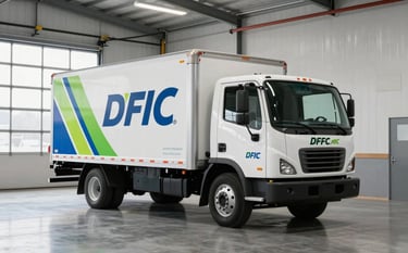 A spacious, modern industrial garage in the North American region. A white commercial transport truck is parked inside, showcasing a clean and vibrant branding application. The lighting is bright, emphasizing the sleek finish and professional execution of the fleet graphics.